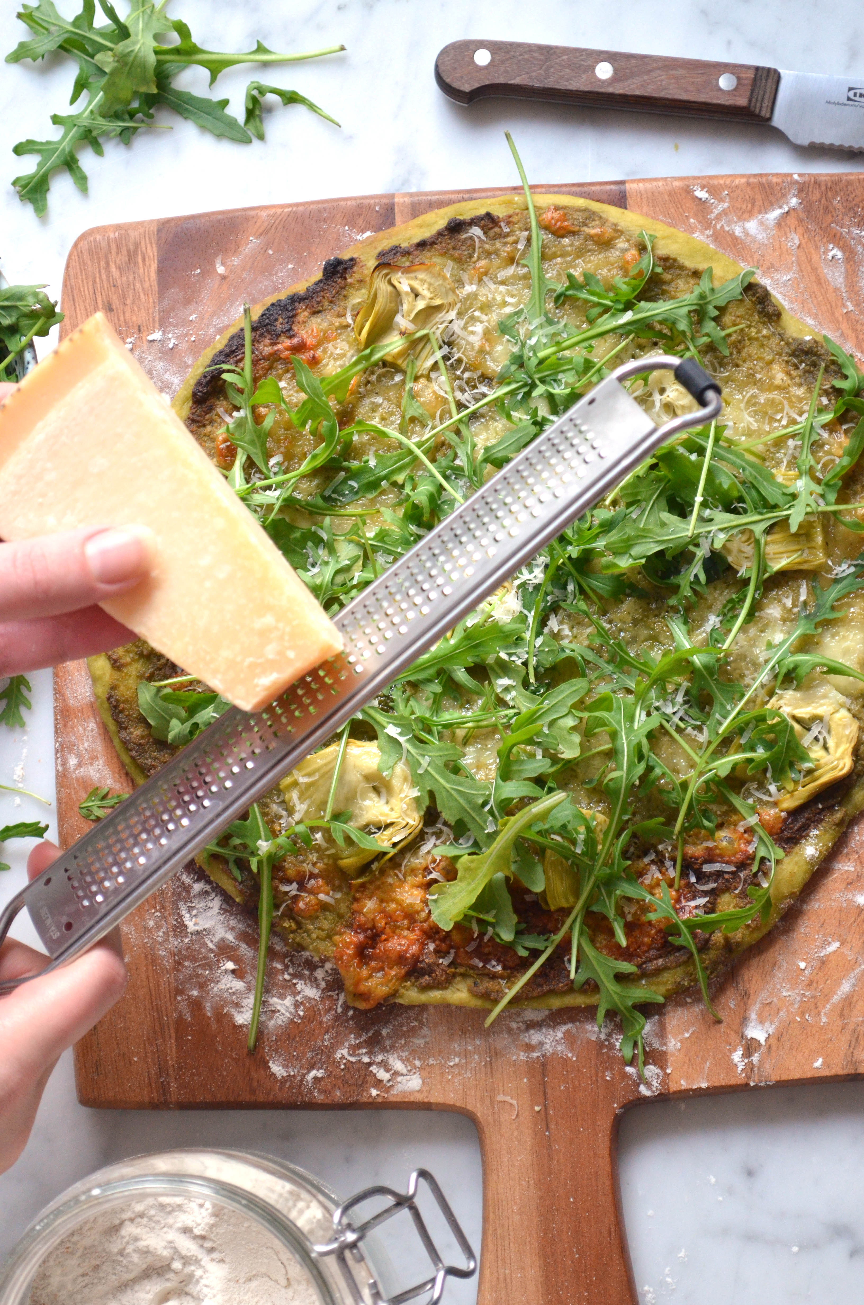 Recipe for homemade pizza dough and pizza verde with pesto, arugula, artichokes, mozzarella and parmesan cheese.
