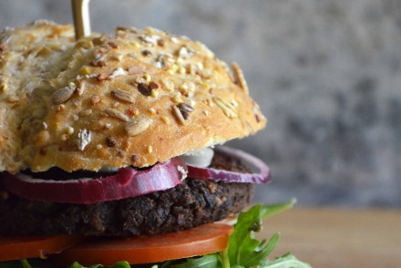 Spicy black bean burger on a bun with red onion, tomato and arugula. Recipe and photo by That Healthy Kitchen
