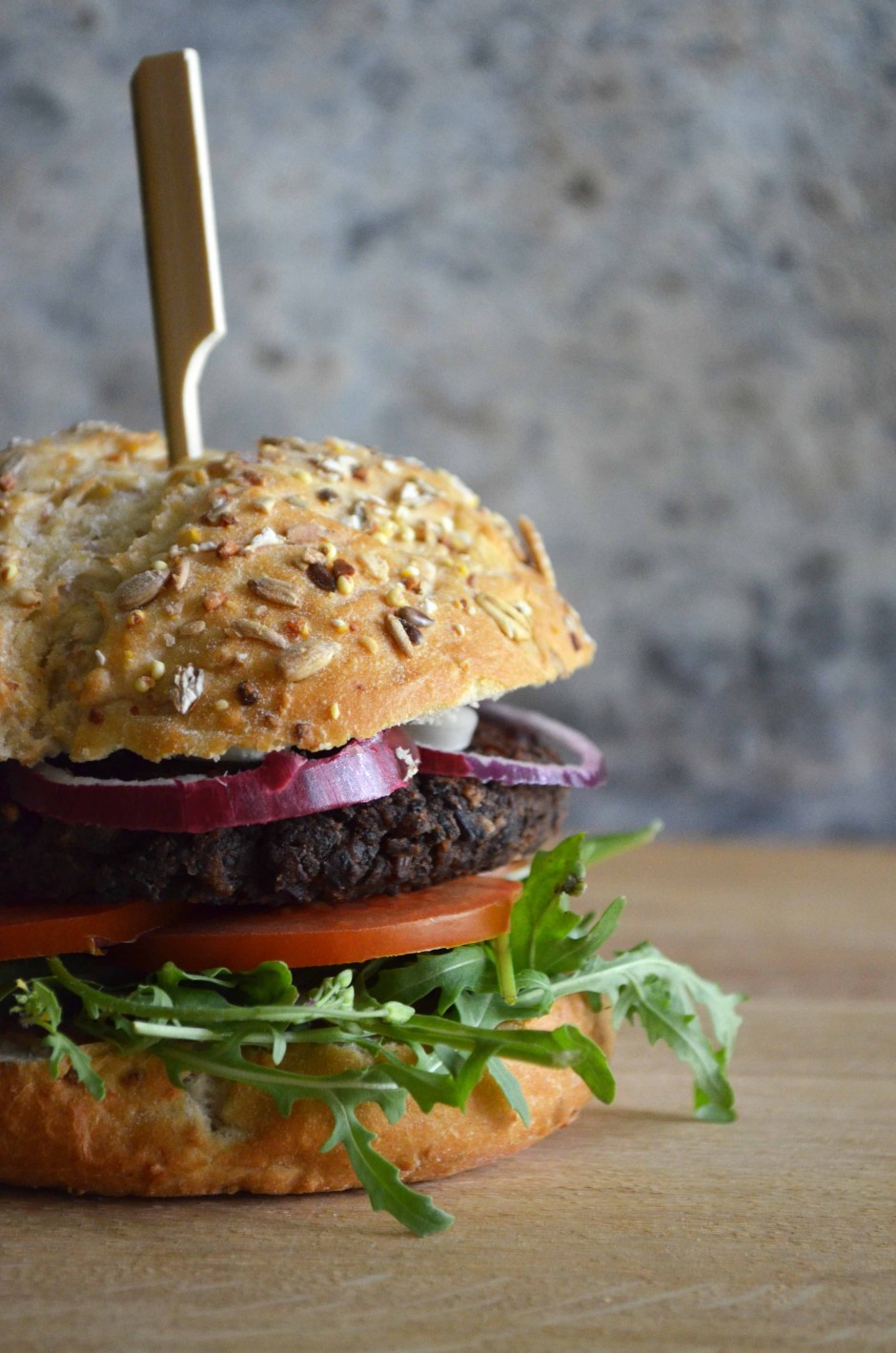 Spicy black bean burger on a bun with red onion, tomato and arugula. Recipe and photo by That Healthy Kitchen