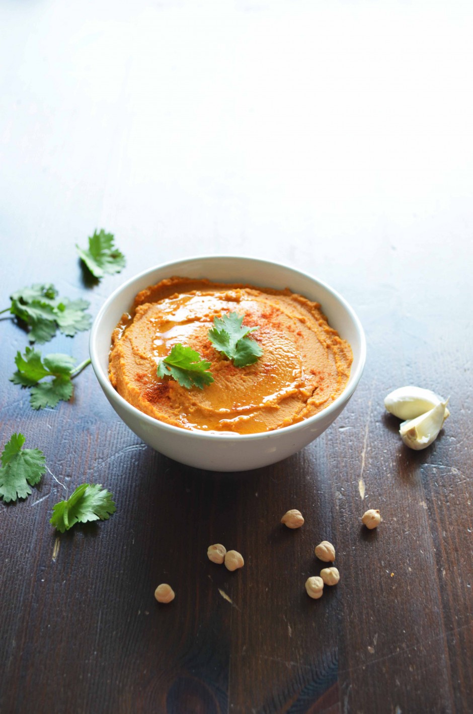 A white bowl filled with grilled red pepper (paprika) hummus, topped with cilantro. Recipe and photo by That Healthy Kitchen