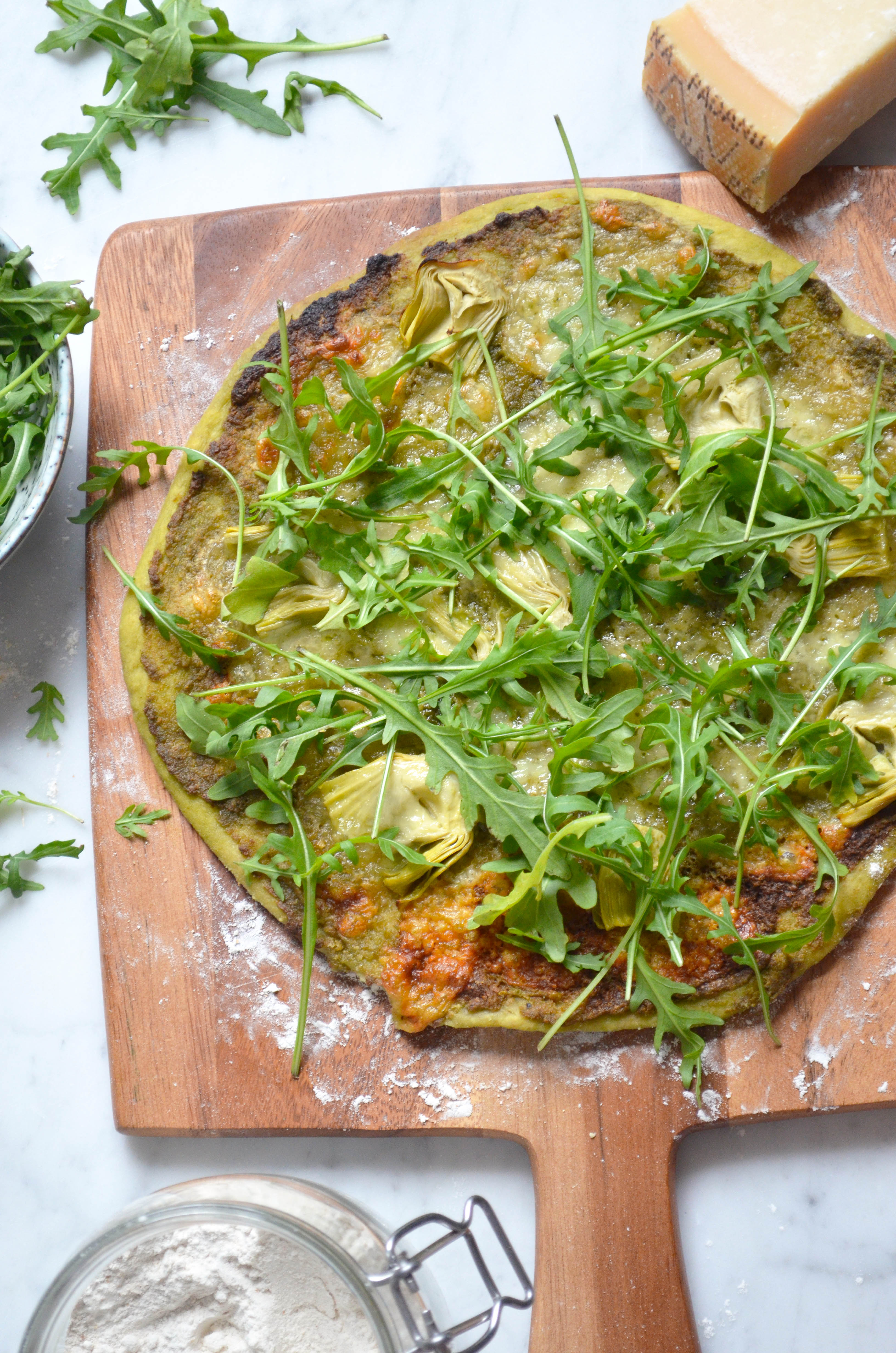 Recipe for homemade pizza dough and pizza verde with pesto, arugula, artichokes, mozzarella and parmesan cheese.