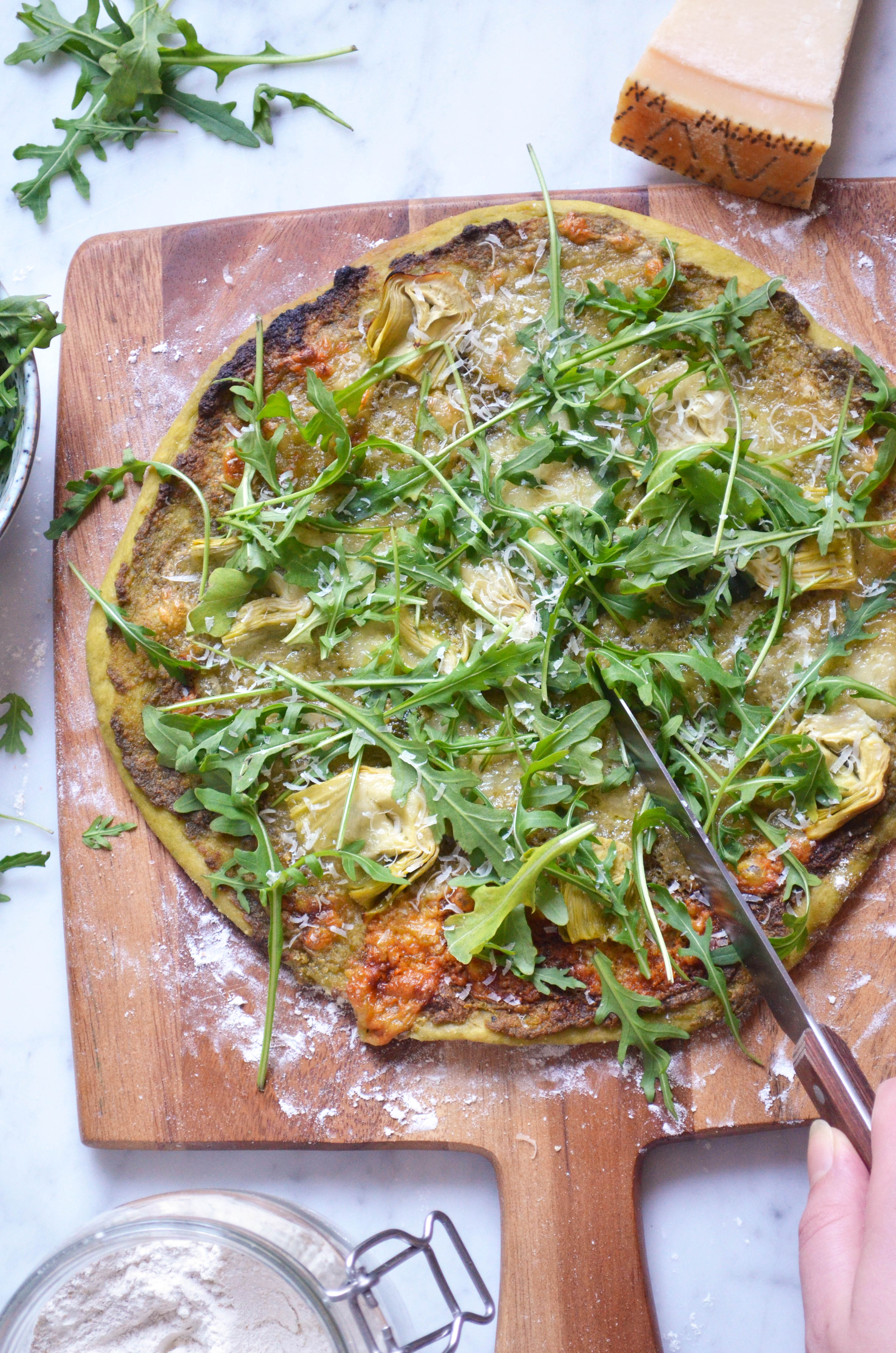 Recipe for homemade pizza dough and pizza verde with pesto, arugula, artichokes, mozzarella and parmesan cheese.