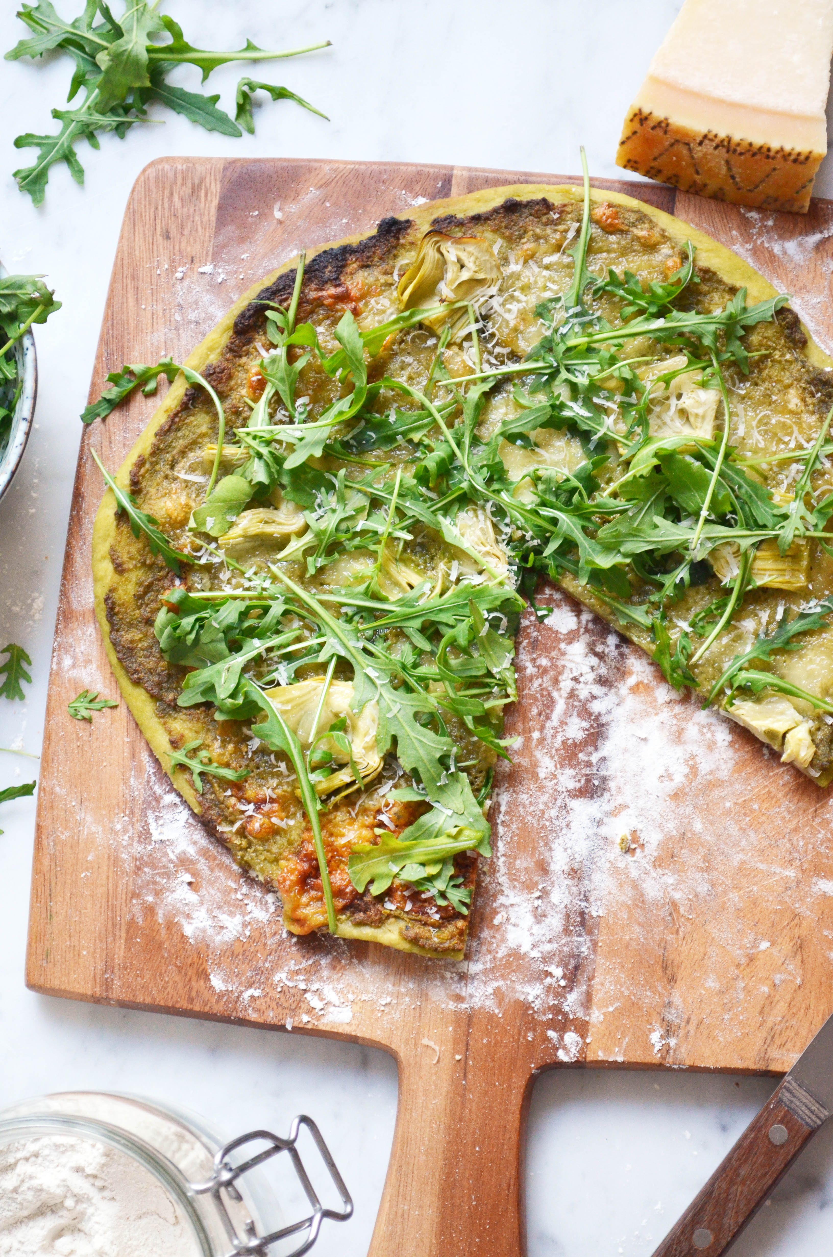 Recipe for homemade pizza dough and pizza verde with pesto, arugula, artichokes, mozzarella and parmesan cheese.